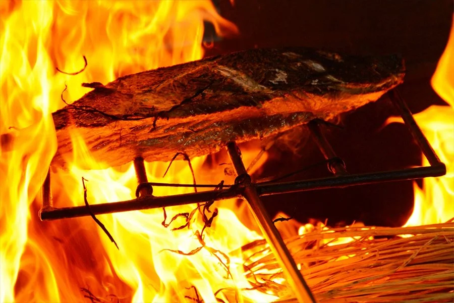 燃え上がる炎の上で藁焼きにされる大きな魚の身