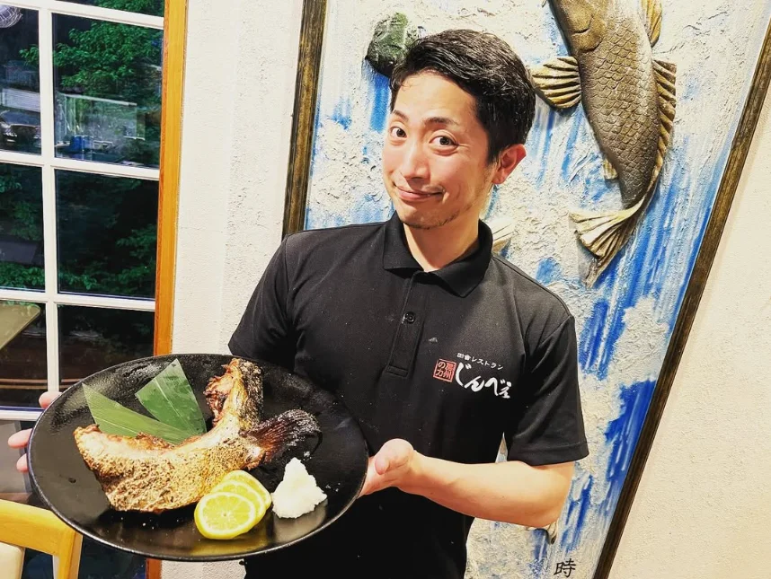 焼き魚の皿を手に笑顔を見せるスタッフ